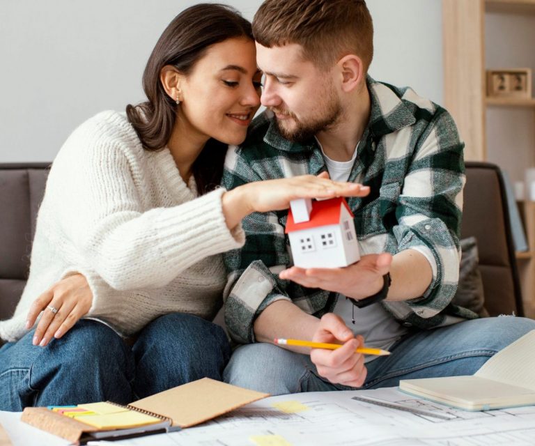 Photo of couple with model house in their hands illustrates blog: 'Homeowners Insurance: What Is Extended Replacement Cost?"