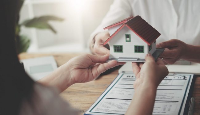 Photo of person holding small house model illustrates blog: "Homeowners Insurance: What Is Loss of Use Coverage?"