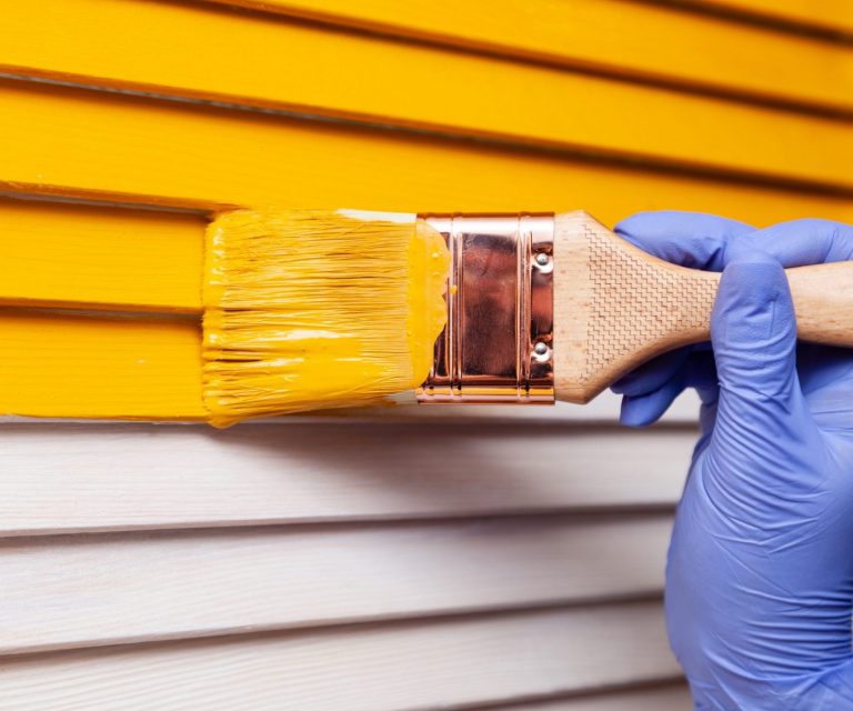Closeup of person painting house illustrates blog "Does Home Insurance Cover Exterior Painting?"