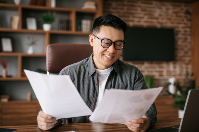 Photo of smiling man looking at documents illustrates blog: "Is Hazard Insurance the Same as Home Insurance?"