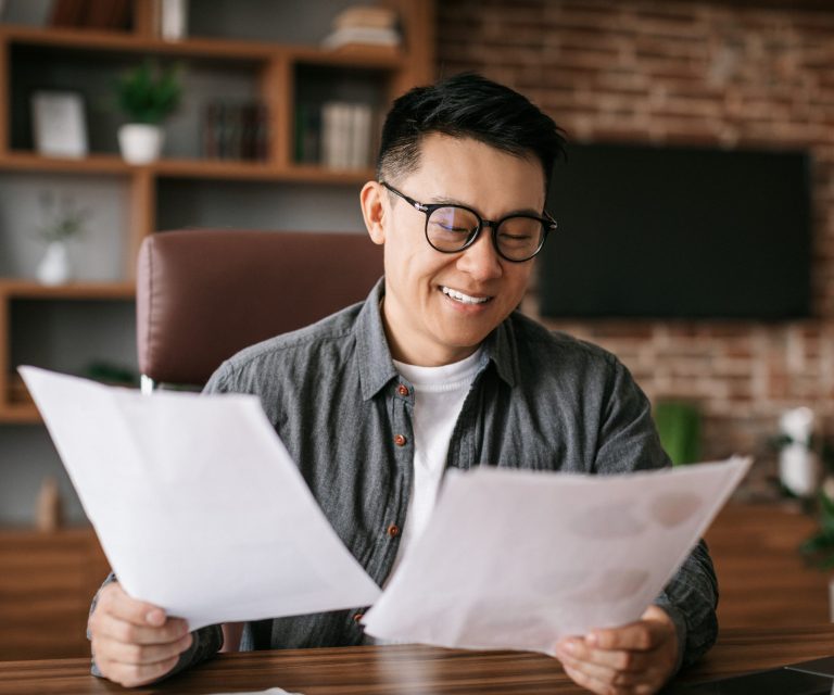 Photo of smiling man looking at documents illustrates blog: "Is Hazard Insurance the Same as Home Insurance?"