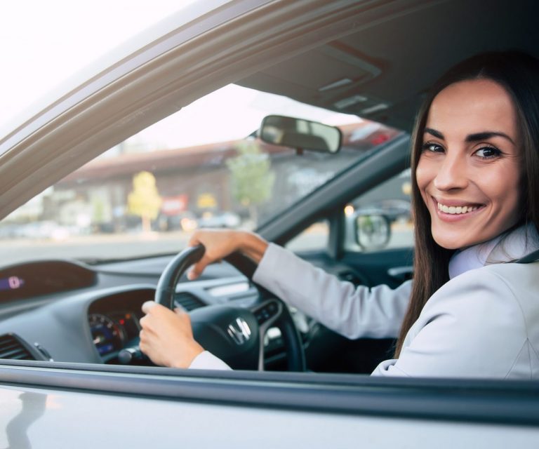 Woman in car holding steering wheel illustrates blog "What Auto Insurance Covers Theft?"