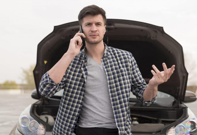 auto-insurance-fp Man talking on the phone with car with open hood behind him illustrates blog Can My Auto Insurance Drop Me?