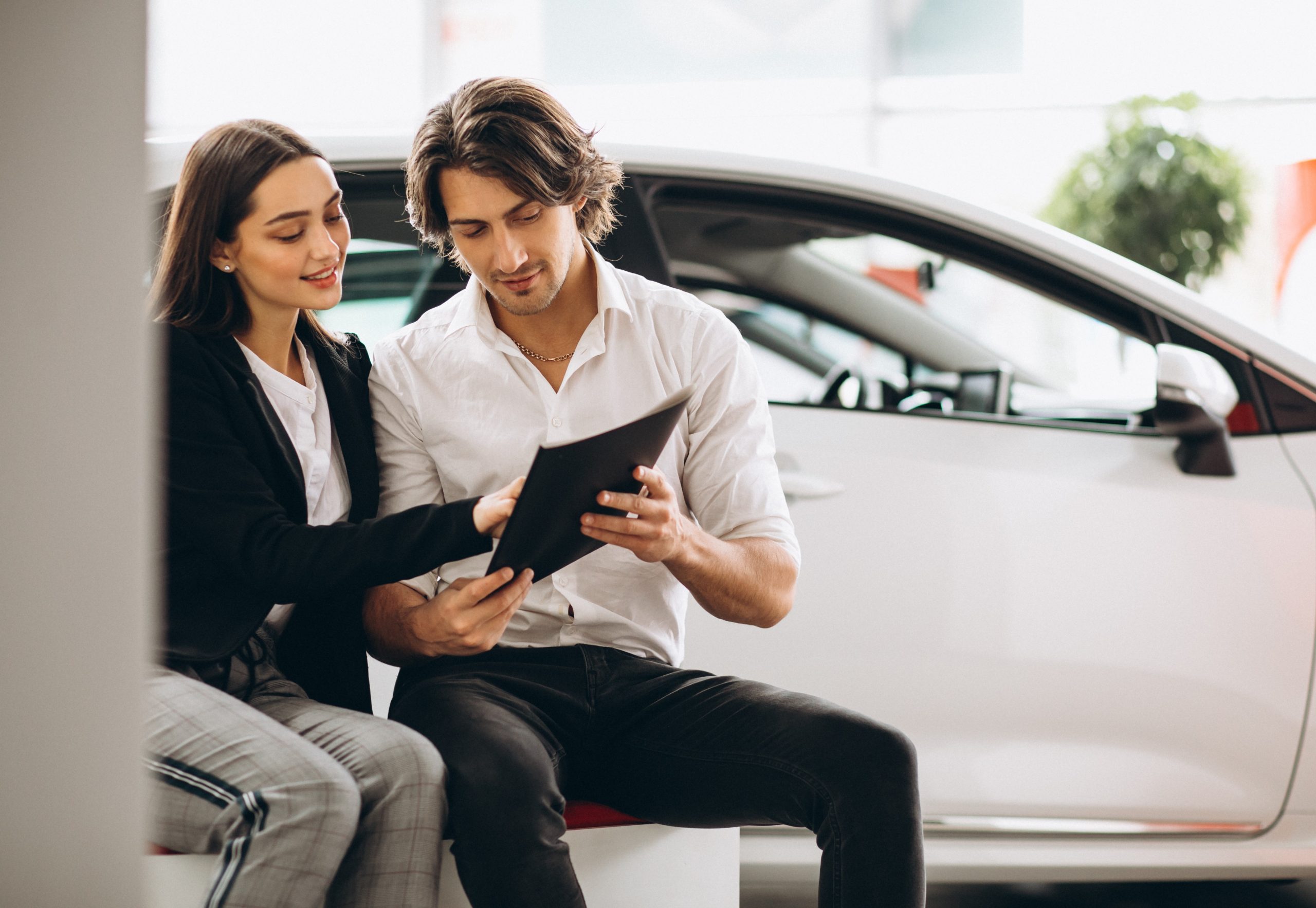 Couple looking at clipboard with car in the background illustrates blog "Can Auto Insurance Be Backdated?"