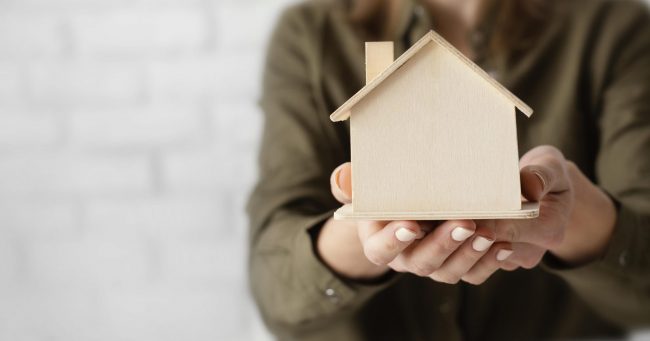 home-insurance-fp Woman holding wooden model of house illustrates blog "Can Home Insurance Be Transferred to a New Owner?"