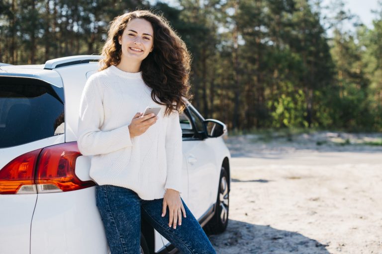 insurance-without-car Young woman leaning against white car illustrates blog "Can You Get Auto Insurance Without a Car?"