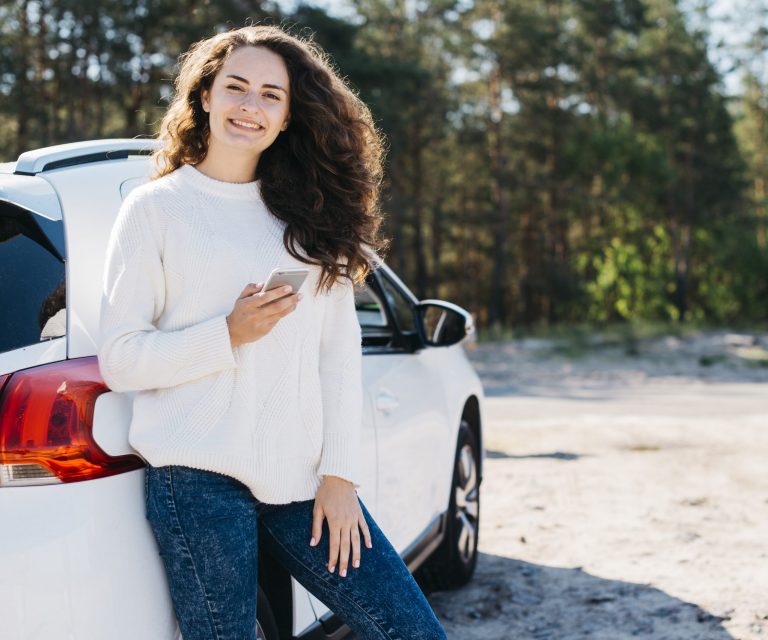 Young woman leaning against white car illustrates blog "Can You Get Auto Insurance Without a Car?"