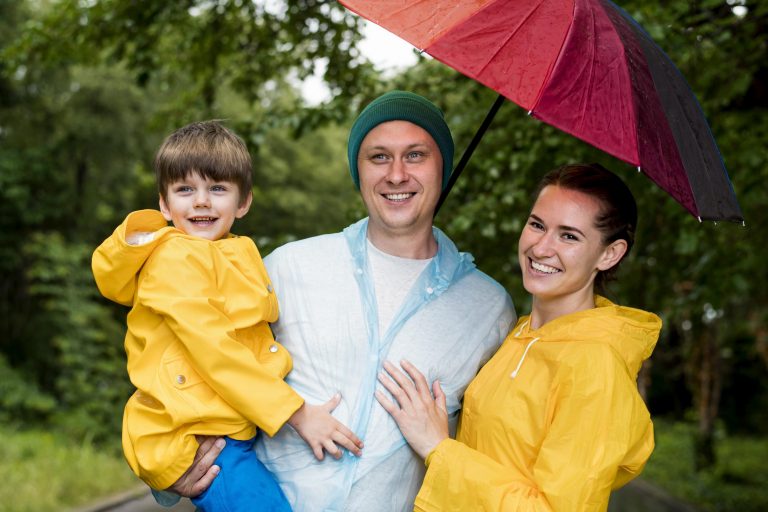 Father, mother, and child posing under umbrella illustrate blog "Does Umbrella Insurance Cover Earthquake Damage?"